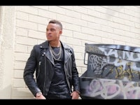 a man in a leather jacket leaning against a wall