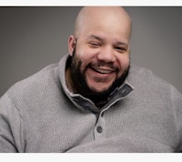 a bald man wearing a gray sweater and smiling