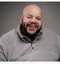 a bald man smiling in a gray sweater