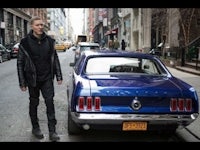 a man standing next to a blue mustang